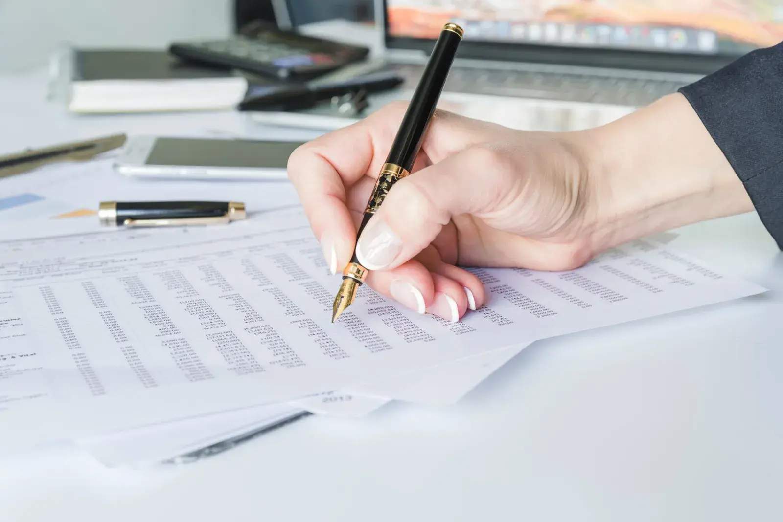 A hand holding a fountain pen over a printed schedule of figures